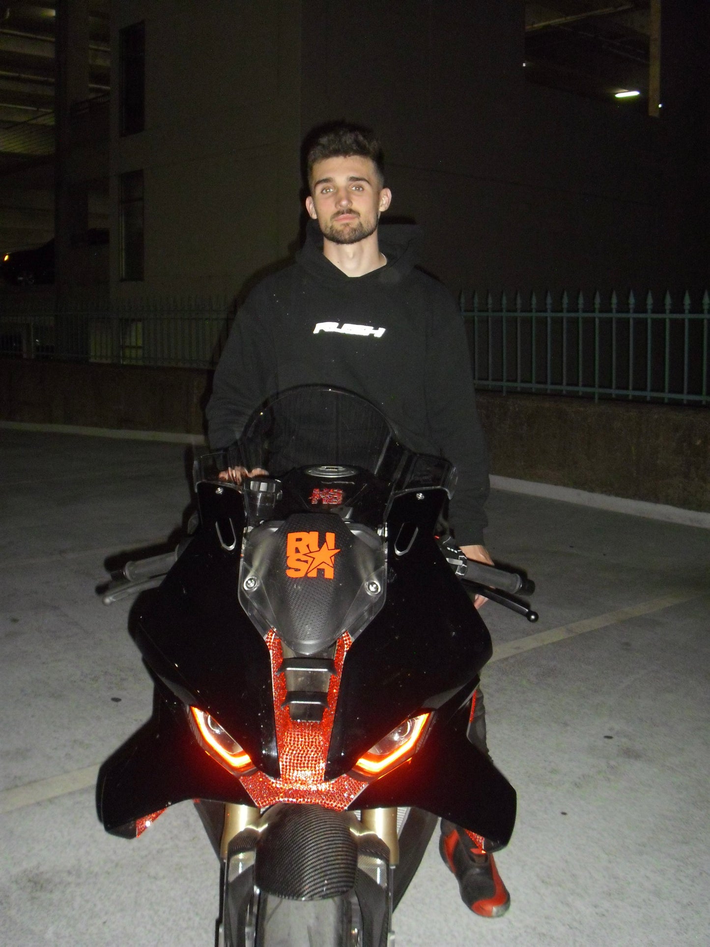 Man sitting on a motorcycle at night with illuminated front lights.