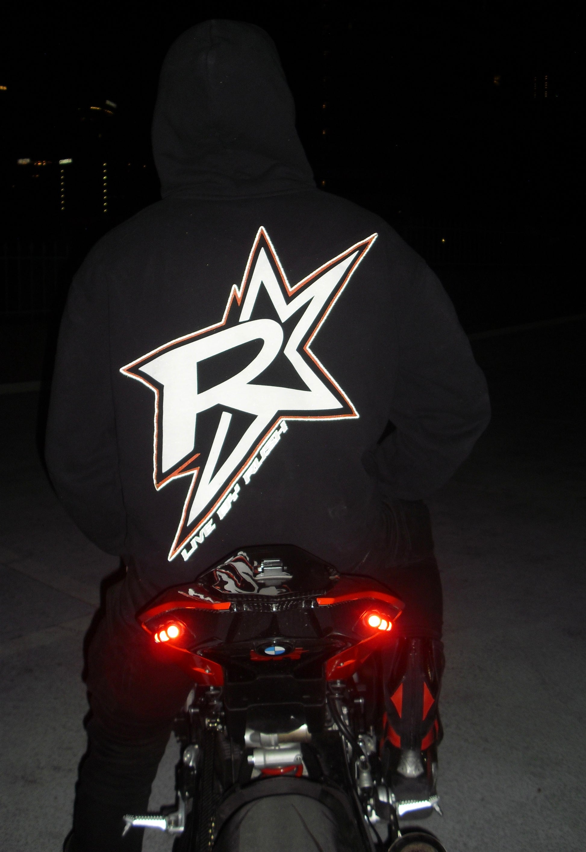 Person wearing a hoodie with a logo on a motorcycle at night